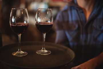 Bar tender holding a tray with glasses of red wine