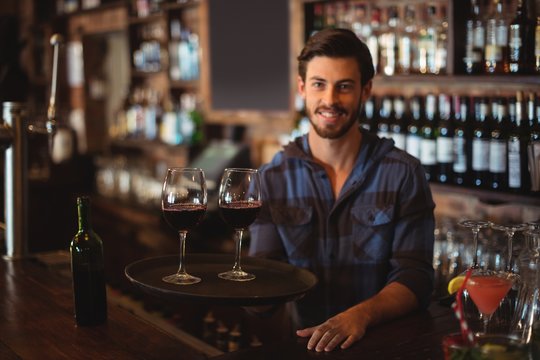 Portrait of bar tender holding a tray with glasses of red wine