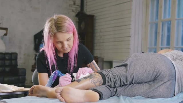 Female tattoo artist with pink hair making tattoo in studio