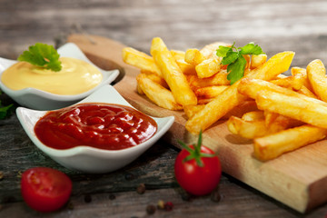 French fries on chopping board with cherry tomato, tomato sauce and mayonnaise in bowls