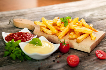 French fries on cutting board with cherry tomato, tomato sauce and mayonnaise in bowls