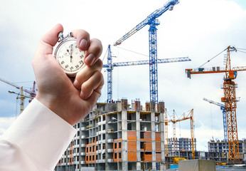 Buildings with cranes and stopwatch in male hand