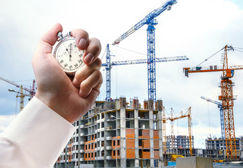 Buildings with cranes and stopwatch in male hand