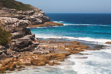 Crowds of tourists relaxing and sunbathing by a  cliff in Tamarama beach in a sunny afternoon of...