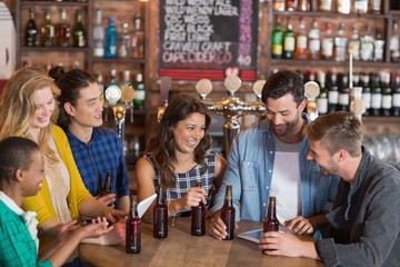Happy young friends with beer bottles standing around table