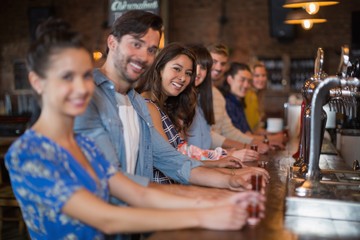 Smiling friends holding short glasses on counter in bar