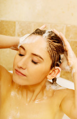 Naklejka premium Young relaxing woman washing hair in bath 