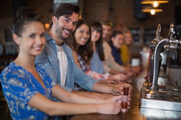Happy friends holding short glasses on counter in bar