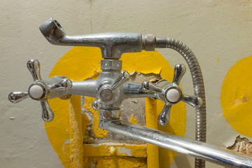 Old rusty shower tap on the background of a painted concrete wall with cracked paint. Poverty