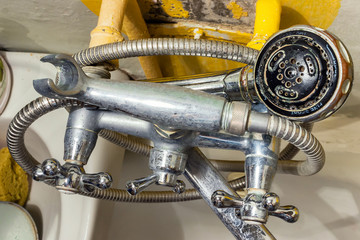 Old rusty shower tap on the background of a painted concrete wall with cracked paint. Poverty