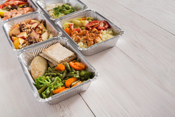 Healthy food take away in foil boxes on wood background