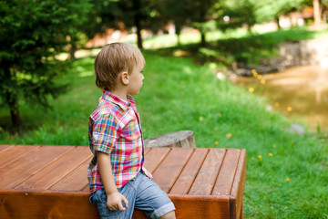 Smiling happy boy sitting on bench near lake. Summer time weekend mood.