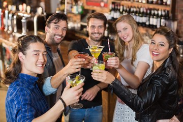 Portrait of happy friends holding drinks while standing in bar