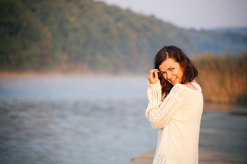 Happy young woman by lake. Feeling relaxed. Enjoying the morning and nature.