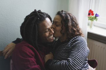 Woman kissing man on cheek while sitting on armchair at home