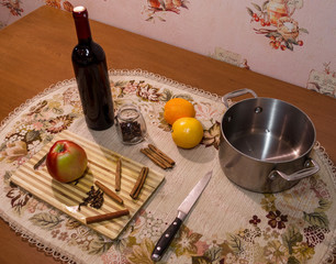 Mulled wine preparation. Red wine, clove, cinnamon, sliced orange, sliced apple in pot and other spices on the cooking board on wooden table it kitchen. Top side view