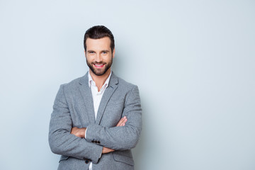 Portrait of happy with beaming smile freelancer in gray jacket standing with crossed hands against...