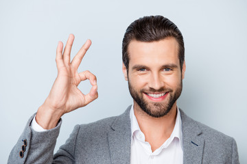 Close up photo of happy man with stylish hairdo and in formalwear showing ok-sign on gray background