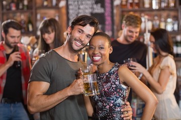 Portrait of young couple embracing while holding beer mugs