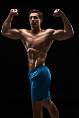 Muscular and fit young bodybuilder fitness male model posing over black background.