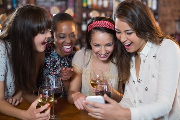 Happy female friends with wineglasses using mobile phone
