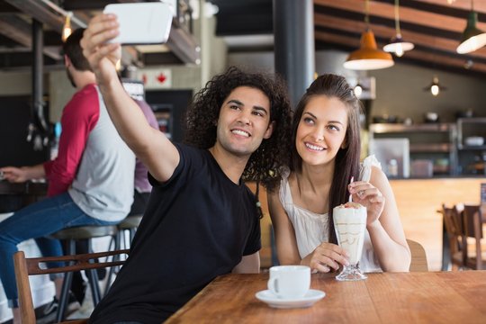 Happy couple taking selfie while sitting in restaurant