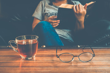 A glass of tea on table with woman reading book on sofa
