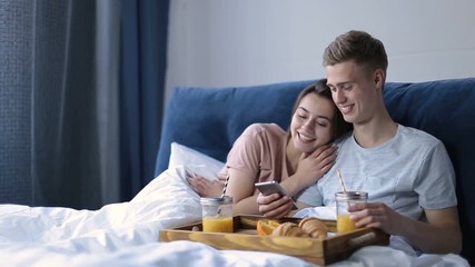 Cheerful couple enjoying romantic breakfast in bed - Powered by Adobe