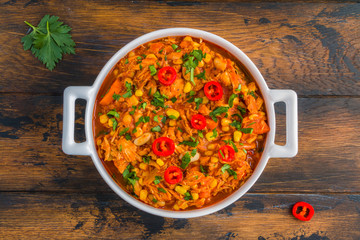 Southwestern homemade chicken and bean stew in a white casserole on the wooden table, top view.