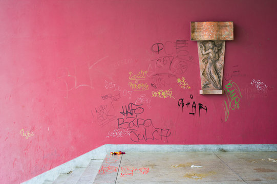 Defacement and vandalism on public space - wall is defaced and painted by spray. Mess and clutter on the ground. Historical relief on the side