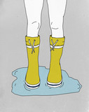 Low section of woman wearing rubber boots while standing in puddle
