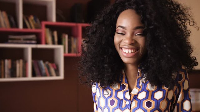Portrait of a beautiful young afro american woman with curly hair turns her head looking into the camera and smiling in a cafe