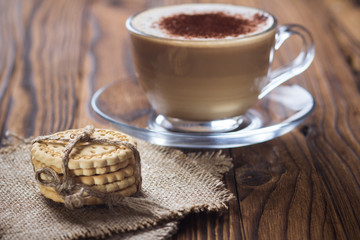 A cup of coffee and small cookies on an antique wooden table