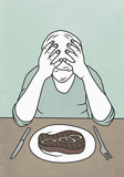 Man with head in hands sitting at dining table behind steak on plate