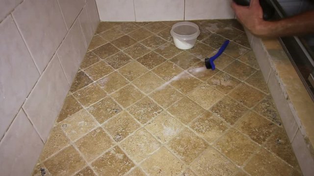 Person Scrubbing Shower Tile Floor. One adult male cleaning grout in a shower tile floor. Low view of a man cleaning a shower tile floor with hydrogen peroxide, baking soda and a small scrub brush