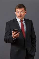 Confident mature businessman standing in front of a grey background and speaking on the sell phone