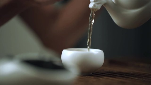 Puring tea pot and cup. Woman hand take teapot. Afternoon tea pouring. Female hand pouring tea drink in porcelain bowl. Close up of woman pure tea cup