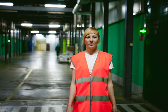 Female Employee In An Orange Robe Vest In The Working Space Of A Production Facility, Exercises Control In Warehouse Production Areas