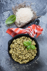 Risotto with spinach in a frying pan over grey stone background, high angle view, vertical shot