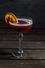 Cocktail with foam in a transparent glass on a high leg, decorated with a dried citrus slice