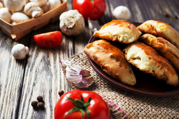 Hearty and tasty food, national Ukrainian cuisine, pies made of yeast dough with mushrooms, tomatoes and spices on rushnyk on a dark rustic wooden background  