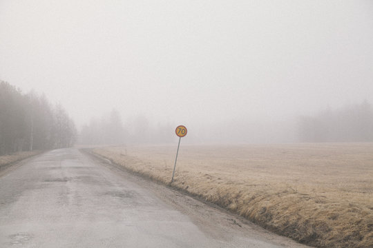 Country road by field in foggy weather against sky
