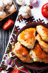 Hearty and tasty food, national Ukrainian cuisine, pies made of yeast dough with mushrooms, tomatoes and spices on rushnyk on a dark rustic wooden background  