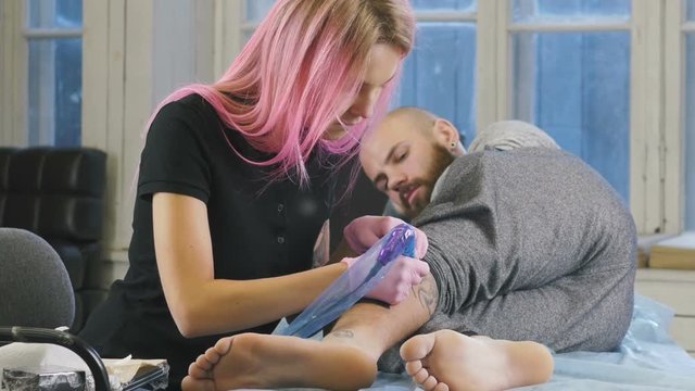 Female tattoo artist with pink hair making tattoo in studio