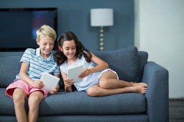 Happy siblings sitting on sofa and using tablet 
