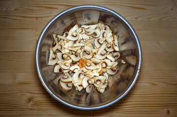 Sliced champignon mushrooms in bowl on wooden desk table background. Flat lay.