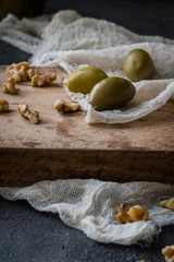 Green olives and walnuts on old wooden board on a dark rustic background. Accompanying snack or appetizer