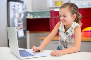 Smiling girl using laptop in kitchen