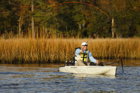 Caucasian man fly fishing in kayak on river