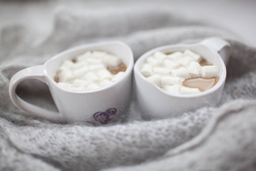 two white mugs with marshmallow on the background wool scarf